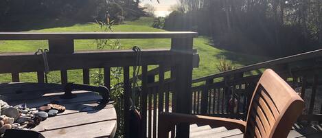 Une terrasse en bois avec une table et des chaises, donnant sur un espace verdoyant bordé d’arbres.