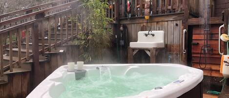 A hot tub with a wooden deck and a wooden cabin in the background.