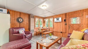Una habitación acogedora con paredes de madera, una mesa de comedor, sofás de cuero y un refrigerador.