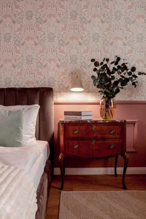Una camera da letto con un letto, un comodino con una lampada, un vaso con una pianta e un libro intitolato “Leaders in Style”.