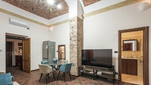 A living room with a TV, dining table, chairs, and a stone accent wall.