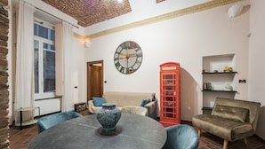 A room with a round table, chairs, a clock, a red telephone booth, and a sofa.