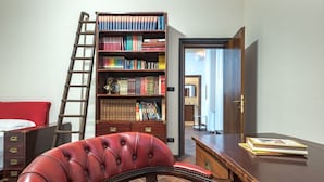A room with a wooden desk, a red leather chair, a bookshelf, and a ladder.