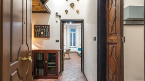 A hallway with wooden doors, a tiled floor, and a view into a room with a window and a sofa.