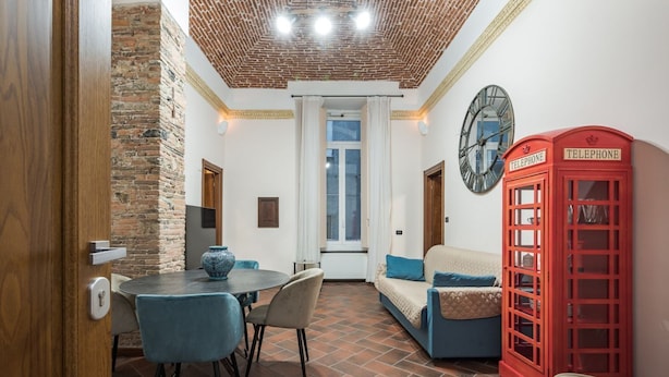A room with a brick wall, a round table with chairs, a red telephone booth, and a sofa with cushions.