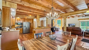 Een rustiek interieur met een houten eettafel, stoelen, een keuken met apparatuur, en een gezellige zithoek met een bank en televisie.