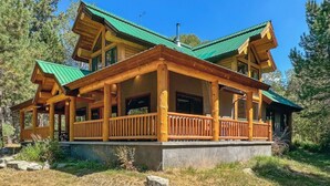 Een chalet met twee verdiepingen, een groen dak, een houten terras en een stenen fundering.