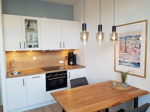 A modern kitchen with white cabinets, a wooden countertop, a built-in oven, and a coffee machine.