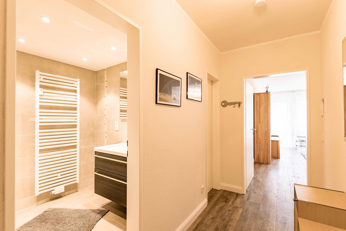 A hallway with a wooden floor, a door with a key hook, and a framed picture on the wall.