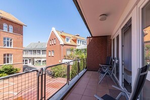 Ein Balkon mit Blick auf angrenzende Gebäude, einem Metallgeländer und einer Tür, die zu einem Innenraum führt.