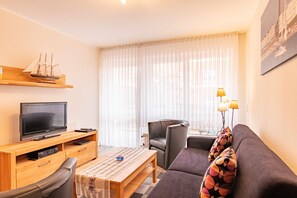 A modern living room with a flat-screen TV, wooden furniture, a sofa, a chair, and a ship model. - Komfortable, Ruhige und Zentral Gelegene Ferienwohnung Seeschwalbe auf Borkum - Strandstraße 5-7 (Borkum)