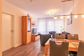 Un salon moderne avec un meuble en bois, un téléviseur, une table à manger avec des chaises et une grande fenêtre avec des rideaux.
