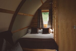 A bedroom with a sloped ceiling, a bed with white bedding and brown pillows, and a window with curtains. - Ensuite Cabin with Stunning Brecon Beacons Views (Brecon)