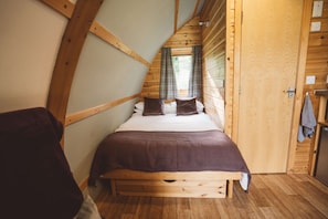 A wooden room with a bed, a window with curtains, and a door.