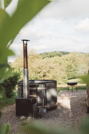 A wood stove with a chimney, a seating area, and a view of a forested hillside. - Hot Tub Cabin With Views Over The Brecon Beacons (Brecon)