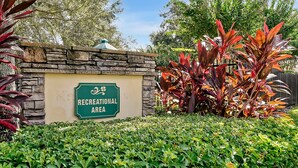 A stone wall with a sign reading "Recreational Area" surrounded by lush greenery and plants. - 3BR Heated Pool+Spa | Movie Room | Pet-Friendly (Orlando)