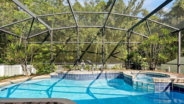 A swimming pool with a glass enclosure, surrounded by lush greenery and a white fence. - 3BR Heated Pool+Spa | Movie Room | Pet-Friendly (Orlando)
