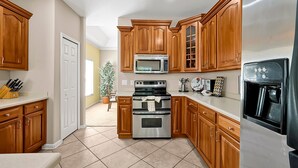 A kitchen with wooden cabinets, stainless steel appliances, and a tiled floor. - 3BR Heated Pool+Spa | Movie Room | Pet-Friendly (Orlando)