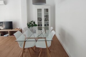 Zona pranzo moderna con tavolo in vetro, sedie bianche e mobile contenitore bianco con ripiani.
