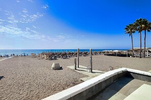 Una spiaggia con ombrelloni di paglia, sdraio e palme.