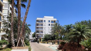 A modern multi-story building with balconies, surrounded by palm trees and a paved walkway. - Apartment in the center of Estepona (Estepona)