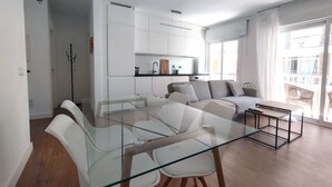 A modern apartment with a glass dining table, a grey sofa, and a kitchen area with white cabinets. - Apartment in the center of Estepona (Estepona)