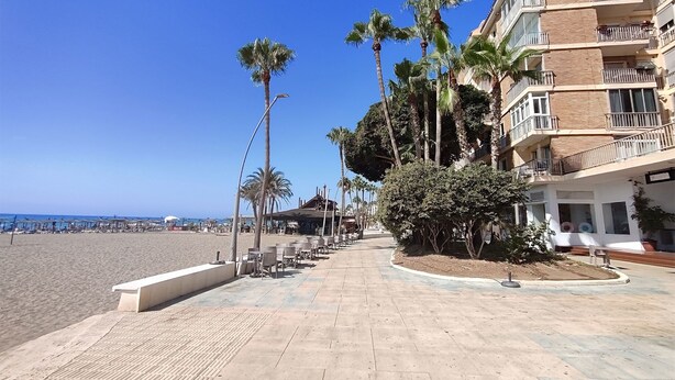A beachfront promenade with palm trees, outdoor seating, and a building with balconies. - Apartment in the center of Estepona (Estepona)