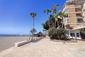 A beachfront promenade with palm trees, outdoor seating, and a building with balconies.