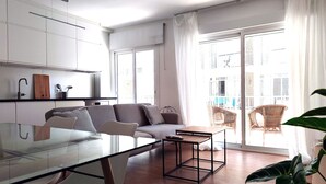 A modern living space with a glass dining table, a grey sofa, wicker chairs, and a large window with curtains. - Apartment in the center of Estepona (Estepona)