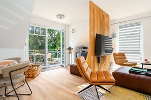 Una sala de estar moderna con un amplio ventanal corredera, un televisor de pantalla plana montado en un panel de madera, sofás de cuero y una zona de comedor con mesa y sillas.