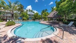 A swimming pool with a 3 FT depth sign, surrounded by lounge chairs, palm trees, and a thatched-roof structure. - 3-bedroom townhome in Key West with fitness room, WiFi (Key West)