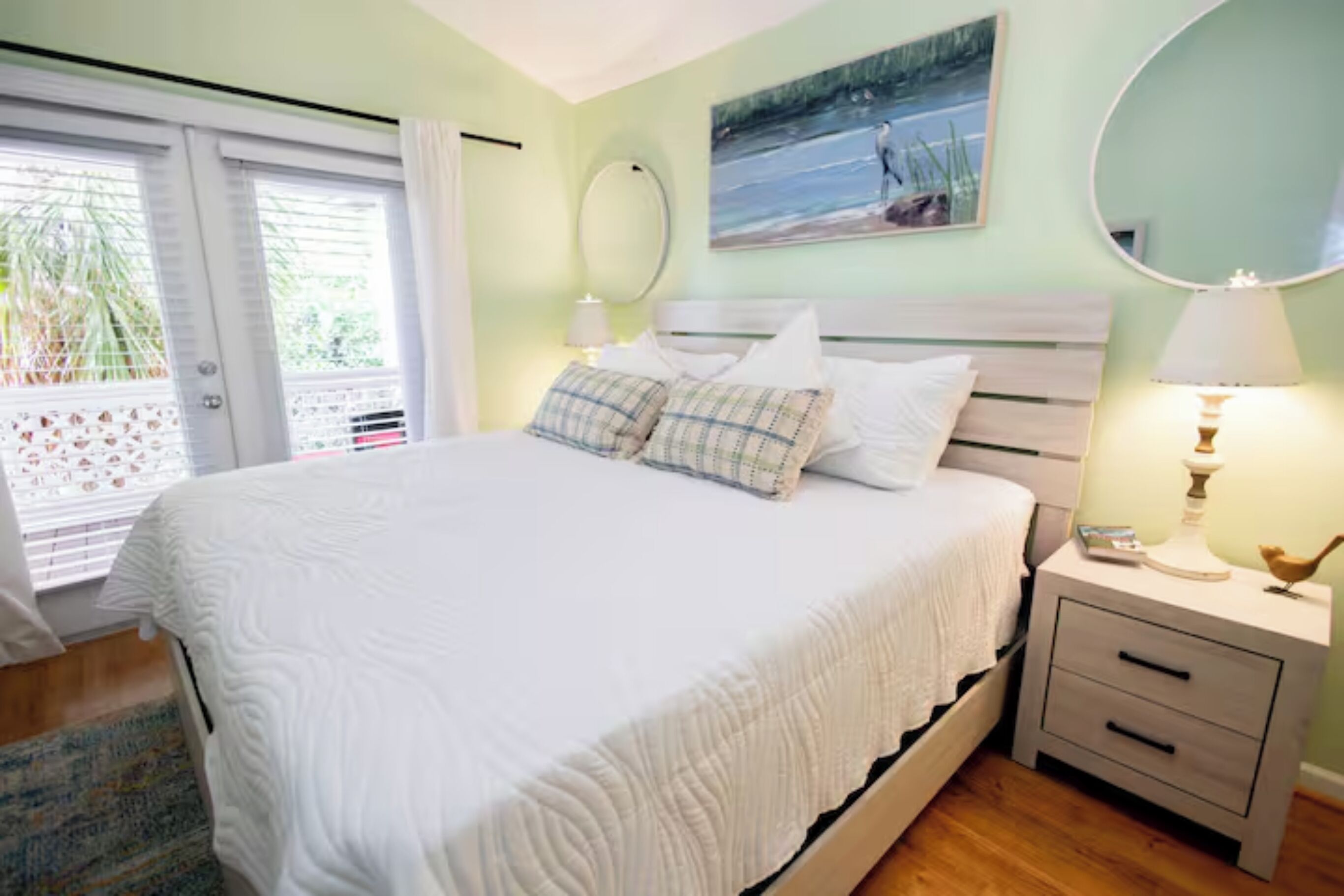 A bedroom with a bed, a nightstand with a lamp, a mirror, and a painting on the wall.