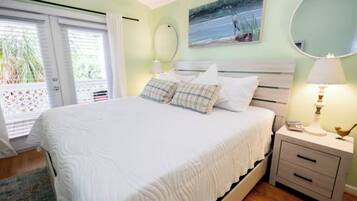 A bedroom with a bed, a nightstand with a lamp, a mirror, and a painting on the wall.