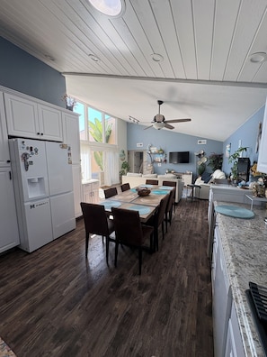 A kitchen with a dining area, wooden flooring, a ceiling fan, and a refrigerator.