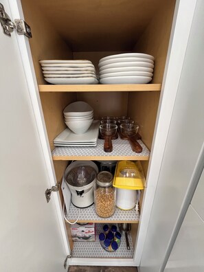 Una despensa de cocina con estantes que contienen platos, tazones y frascos.