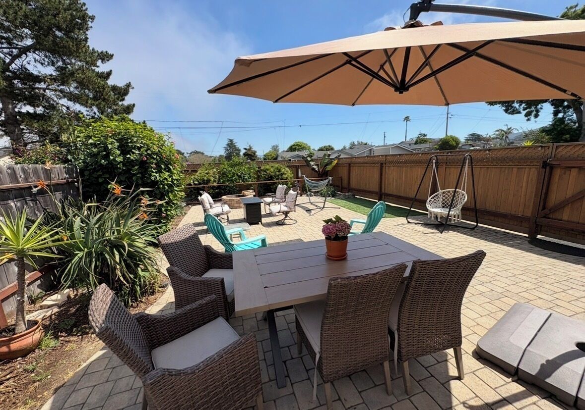 An outdoor patio with wicker furniture, a table, and a large umbrella.