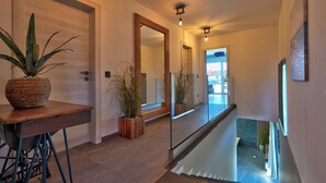A modern hallway with a wooden table, potted plants, a large mirror, and a glass railing leading to an upper level. - Villa BAVIGO (Istria - Marcana) (Marcana)