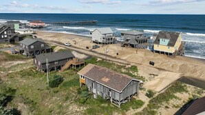 A coastal area with houses on stilts, a pier extending into the ocean, and a sandy beach. - 7038- Hunky Dory - Rodanthe Beach Cottage | 58 Yards to Beach (Rodanthe)