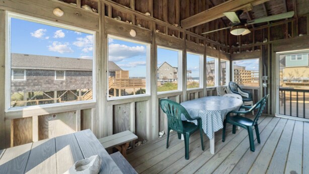 A covered outdoor deck with a table and chairs, large windows, and a view of buildings. - 7038- Hunky Dory - Rodanthe Beach Cottage | 58 Yards to Beach (Rodanthe)