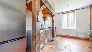 Eine Küche mit Fliesenrückwand, Holzbalken, gefliestem Boden und einem Fenster mit Vorhängen.