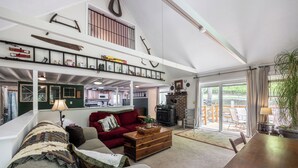 Een ruime woonkamer met een hoge plafond, een open haard en een balkon met zitplaatsen.