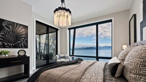 A bedroom with a large bed, a chandelier, a painting, and a view of the mountains. - Waterfront Luxe Seasons ~8~ Boat Slip (Sandpoint)