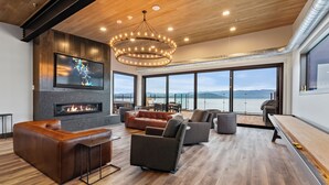 A modern living room with a fireplace, comfortable seating, and large windows offering a scenic view. - Waterfront Luxe Seasons ~8~ Boat Slip (Sandpoint)