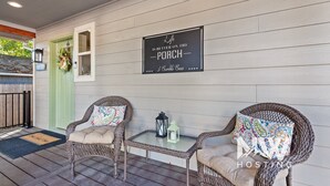 A porch with wicker chairs, a small table, and a sign reading "Life is better on the porch - 3 Bumbles Bees". - Two-Story Midtown Home—Newly Renovated, Fire Pit, and Peaceful Outdoor Space for Relaxation! (Coeur D Alene)