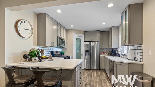 A modern kitchen with a central island, stainless steel appliances, and a clock on the wall. - Two-Story Midtown Home—Newly Renovated, Fire Pit, and Peaceful Outdoor Space for Relaxation! (Coeur D Alene)