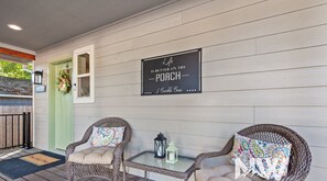 A porch with wicker chairs, a small table, and a sign reading "Life is better on the porch - 3 Bumbles Bees".