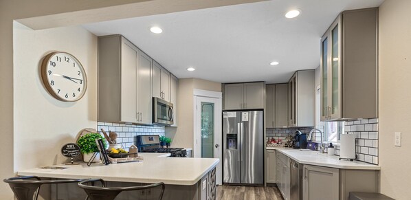 A modern kitchen with a central island, stainless steel appliances, and a clock on the wall.