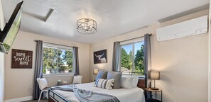 A bedroom with a bed, two windows, a ceiling light, a wall-mounted air conditioner, and a sign that reads "HOME sweet HOME".