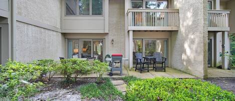 Un immeuble résidentiel à plusieurs étages doté de balcons, d’un petit patio aménagé avec du mobilier d’extérieur et d’un jardin planté de différentes espèces.