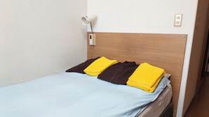 A single bed with a wooden headboard, a light blue bedspread, and two pillows, one brown and one yellow. - Hotel Frontier (Isinomaki)